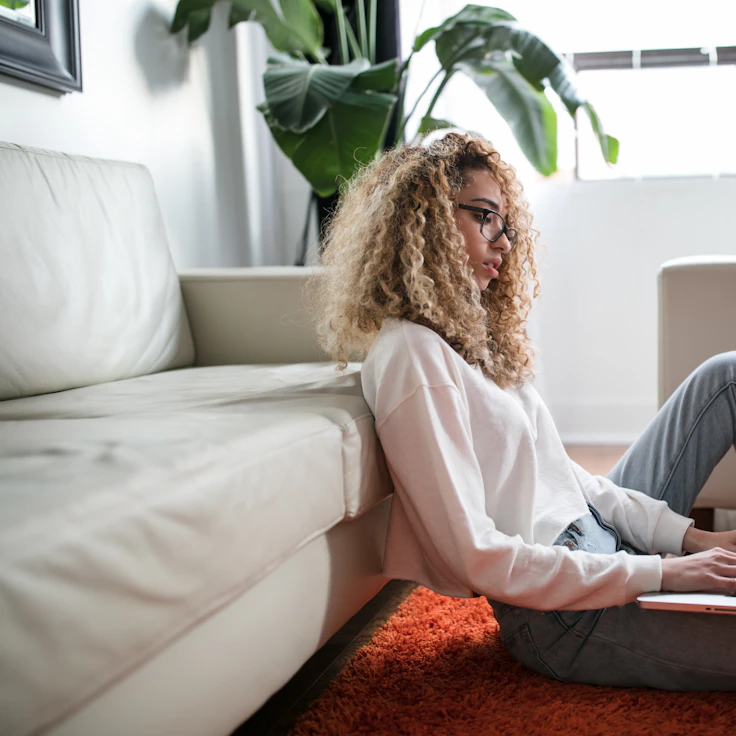 Person sitting on the floor against a couch working on a laptop