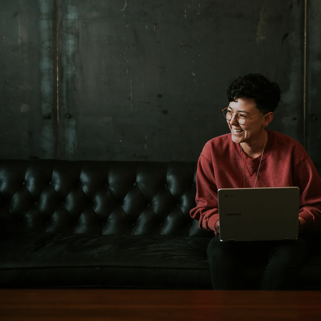 Smiling person using a laptop on a dark leather sofa
